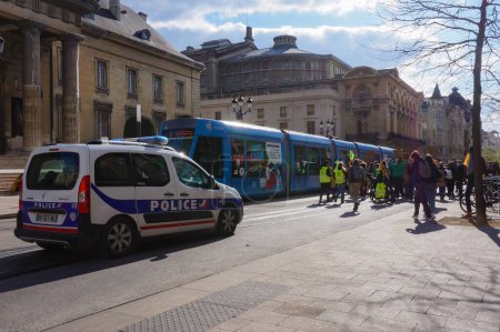 Photo for Reims, France - March 2021 - Escorted at the back by a police car, young, ecologist activists block a tramcar on Rue de Vesle, during a manifestation against global warming and climate change - Royalty Free Image