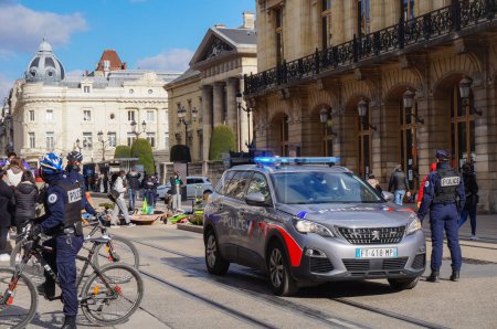 Foto de Reims, Francia - Marzo 2021 - Policías en bicicleta, en la plaza Myron Herrick, y un nuevo Peugeot 5008 de la Policía Nacional, con luces azules encendidas, asegurando una manifestación en la calle de Vesle - Imagen libre de derechos