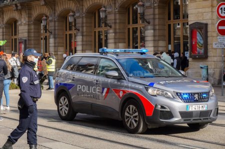 Photo for Reims, France - March 2021 - A female police officer next to the brand-new Peugeot 5008 of the National Police, with blue flashing lights on, in intervention on Rue de Vesle during a demonstration - Royalty Free Image