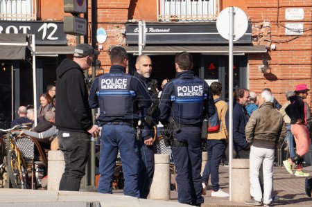 Téléchargez les photos : Toulouse, France - Février 2023 - Un groupe de trois officiers armés de la police municipale de la ville, vêtus de gilets tactiques, patrouille sur la place Saint-Cyprien, au milieu des protestations contre la réforme des retraites - en image libre de droit