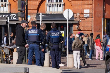 Téléchargez les photos : Toulouse, France - Février 2023 - Un groupe de trois officiers armés de la police municipale de la ville, vêtus de gilets tactiques, patrouille sur la place Saint-Cyprien, au milieu des protestations contre la réforme des retraites - en image libre de droit