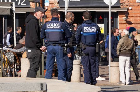 Foto de Toulouse, Francia - Feb. 2023 - Un grupo de tres oficiales armados de la Policía Municipal de la ciudad, vestidos con chalecos tácticos, patrullan en la Plaza Saint-Cyprien, en medio de protestas contra la reforma de las pensiones - Imagen libre de derechos