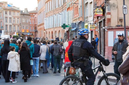 Téléchargez les photos : Toulouse, France - Mars 2023 - Un officier de la police nationale, en vélo, patrouille autour d'une procession catholique pour célébrer l'Annonciation, le jour de la fête des dames, sur la place de la cathédrale - en image libre de droit