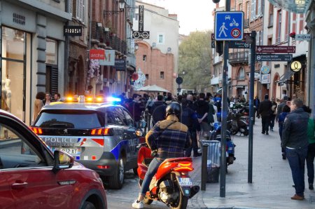 Téléchargez les photos : Toulouse, France - Mars 2023 - Un véhicule de la Police Nationale, tous feux allumés, suit et escorte l'arrière d'une procession catholique dans les rues, à l'occasion de l'Annonciation, le jour de la Fête des Dames - en image libre de droit