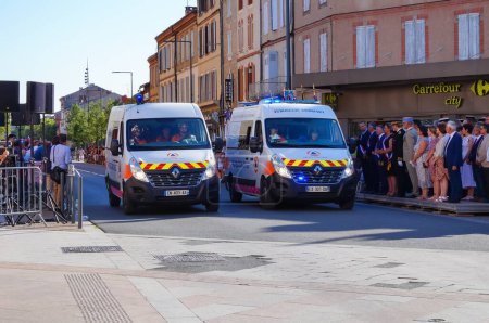 Téléchargez les photos : Albi, France - 14 juillet 2022 - Deux fourgonnettes Renault Sprinter blanches, véhicules d'urgence, de la Croix-Rouge française, défilant dans la rue au milieu des célébrations de la fête nationale - en image libre de droit