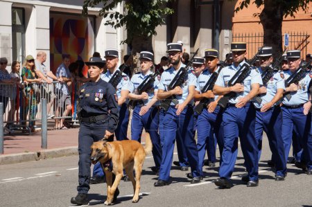 Téléchargez les photos : Toulouse, France - 14 juillet 2023 - Une femme maître-chien de la Gendarmerie (police militaire française) avec un Malinois, et un détachement d'officiers, armés de fusils FAMAS, au défilé de la fête nationale - en image libre de droit
