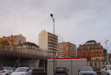 Foto de Troyes, Francia - Oct. 2020 - Coches aparcados junto a la estación de tren, debajo del puente de Rue Voltaire, en el centro de la ciudad, con bloques de torre residenciales en el fondo y farolas todavía iluminadas - Imagen libre de derechos