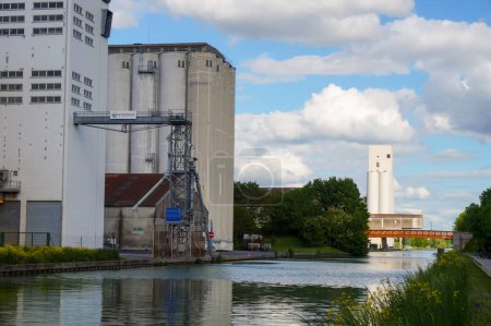 Photo for Reims, France - May 2021 - Grain elevators and industrial factories at the river port of Pre des Moines Quay, by Marne-Aisne Canal, in the Champagne Region, which hosts a powerful agrobusiness - Royalty Free Image