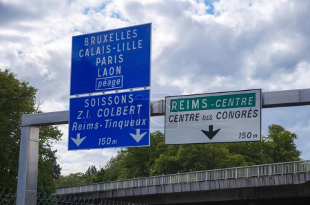 Foto de Reims, Francia - Mayo 2022 - Señal de ruta azul que indica las direcciones de Bruxelles y París (por la autopista, con peaje), y una blanca y verde que indica el centro de Reims y la convención - Imagen libre de derechos
