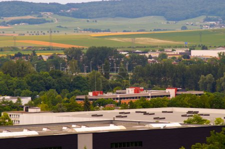 Foto de Reims, Francia - Junio 2021 - Vista superior de los edificios comerciales y las fábricas industriales en el parque empresarial Henri Farman, debajo de los campos agrícolas que se encuentran en la ladera montañosa y boscosa de la montaña Reims - Imagen libre de derechos