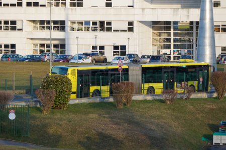 Foto de Reims, Francia - Feb. 2022 - Un autobús urbano articulado y amarillo sirve el Campus Science Moulin de la Housse de la Universidad Reims Champagne-Ardenne (URCA), pasando por el edificio principal de enseñanza blanco - Imagen libre de derechos