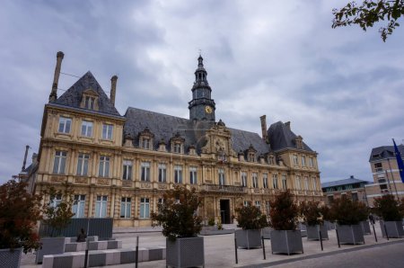 Photo for Reims, France - April 2021 - Potted trees on Simone Veil Esplanade in the forefront, at the foot of the main facade and belltower of the City Hall, a classical edifice built in the 17th century - Royalty Free Image