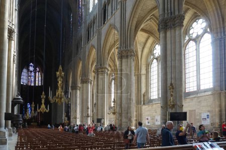Foto de Reims, Francia - Junio 2022 - Los turistas que visitan la nave de la Catedral de Notre-Dame, que tiene lámparas de araña colgando del techo, columnas de piedra, bóvedas de costillas y ventanas arqueadas ampliadas para el ambulatorio - Imagen libre de derechos