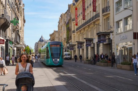 Foto de Reims, Francia - Junio 2022 - Escena urbana típica y paisaje urbano en la Rue de Vesle en verano, una popular y a menudo concurrida calle alta en el centro histórico de la ciudad, con un tren ligero verde de Citura pasando por - Imagen libre de derechos