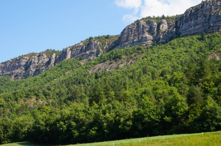 Foto de Impresionantes acantilados rocosos en la cima de las cordilleras que dominan las verdes laderas boscosas, en un hermoso paisaje forestal en Alpes-de-Haute-Provence, en los frondosos Alpes meridionales de Francia, en un día soleado brillante - Imagen libre de derechos