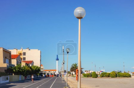 Téléchargez les photos : Narbonne-Plage, France - Août 2020 - Piste cyclable et promenade piétonne le long de la plage, bordée par les bâtiments de la station balnéaire, avec le phare qui domine la marina en arrière-plan - en image libre de droit