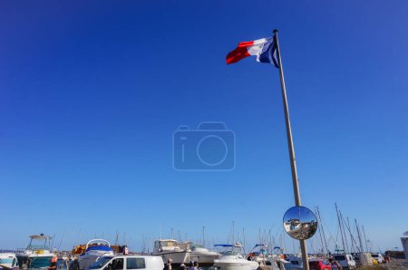 Foto de La bandera nacional de Francia, de tres colores, azul, blanca y roja, ondeó sobre un poste de metal blanco y yates - Imagen libre de derechos