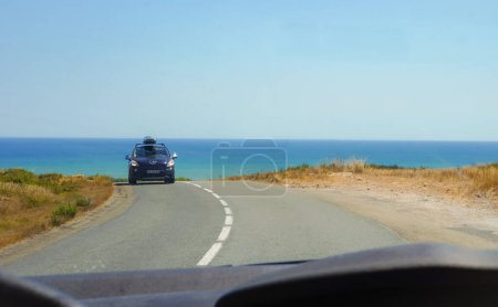 Téléchargez les photos : Narbonne-Plage, France - Août 2020 - Vue d'un autre véhicule, une voiture Prugeot avec un toit conduit sur la route qui mène à la plage ; à l'horizon, l'eau bleue de la mer Méditerranée - en image libre de droit
