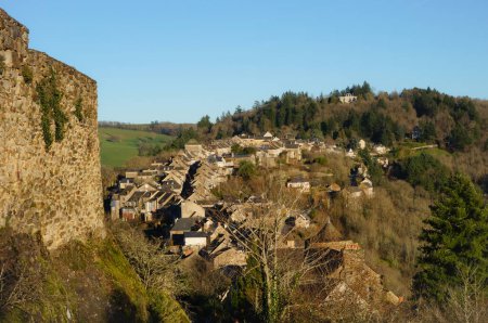 Foto de Vista general del faubourg de la ciudad medieval francesa Najac, vista desde la muralla de piedra de la fortaleza real: la bastide se construye a lo largo de la calle principal, situada en una cresta de colina sobre el bosque de Aveyron - Imagen libre de derechos