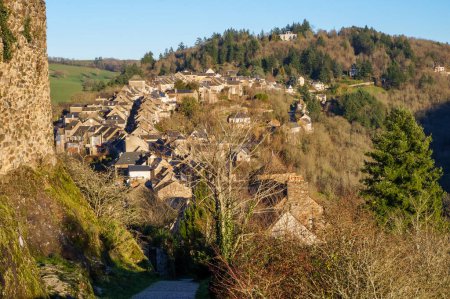 Foto de Vista general del faubourg de la ciudad medieval francesa Najac, vista desde la muralla de piedra de la fortaleza real: la bastide se construye a lo largo de la calle principal, situada en una cresta de colina sobre el bosque de Aveyron - Imagen libre de derechos