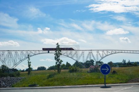 Foto de Tanus, Francia - 1 de agosto de 2022 - Un modelo a escala en una rotonda representa el Viaducto de Viaur, con un tren que pasa por encima; el puente ferroviario actual de principios del siglo XX se encuentra cerca en el valle. - Imagen libre de derechos