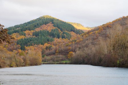 Téléchargez les photos : Vue pittoresque sur le Tarn, coulant au pied d'une colline colorée et boisée à Lincou, un emplacement rural dans l'Aveyron, sud de la France, avec une forêt aux tons automne et hiver - en image libre de droit