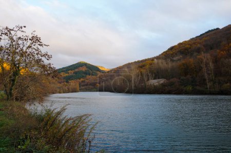 Foto de Pintoresca vista sobre el río Tarn, que fluye al pie de una colorida colina arbolada en Lincou, un lugar rural en Aveyron, al sur de Francia, con un bosque con tonos de otoño e invierno - Imagen libre de derechos