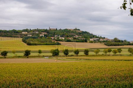 Téléchargez les photos : Paysage rural français avec un joli village sur une colline boisée, entouré de champs, dans le Lauragais par une journée nuageuse - en image libre de droit