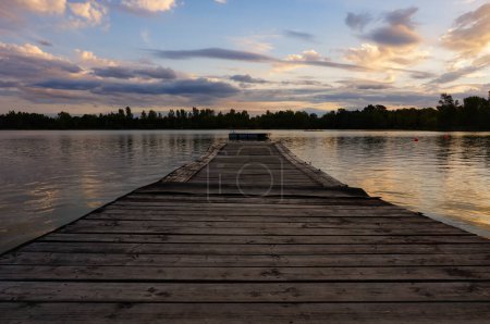 Téléchargez les photos : Belle vue coucher de soleil sur un lac du centre de loisirs des Etangs, à Saix, Sud de la France, avec une jetée en bois flottant sur l'eau et les bois de la réserve naturelle en arrière-plan - en image libre de droit