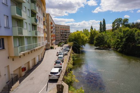 Téléchargez les photos : Castres, France - Août 2020 - Voitures des habitants stationnées au pied d'un quartier résidentiel de logements sociaux, au bord d'un bras de la rivière Agout, bordé d'arbres verdoyants, dans le centre-ville - en image libre de droit
