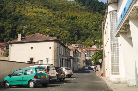 Foto de Mazamet, Francia - Agosto de 2018 - Una calle con plazas de aparcamiento, bordeadas de casas tradicionales, que se dirige al Parque Natural de Haut-Languedoc en la hermosa Montaña Noire, una montaña en el Macizo Central - Imagen libre de derechos