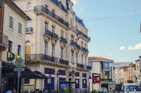 Téléchargez les photos : Mazamet, France - Août 2018 - Élégant bâtiment haussmannien arborant un drapeau français sur un balcon du Cours Ren Reilles, la rue principale du centre-ville de Mazamet, avec des succursales bancaires et des commerces - en image libre de droit