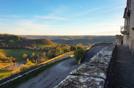 Téléchargez les photos : Panorama impressionnant sur un plateau verdoyant vu depuis les remparts médiévaux de Puycelsi, une ville fortifiée du sud de la France, au-dessus d'une route serpentine de campagne qui serpente autour de la montagne - en image libre de droit