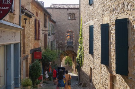 Téléchargez les photos : Cordes-sur-Ciel, France - Août 2021 - Paysage pittoresque dans le village médiéval, avec de vieilles maisons typiques avec des magasins traditionnels, et une porte voûtée construite sous un ancien château fort - en image libre de droit