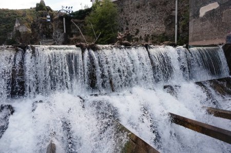 Foto de Potentes caídas de agua con algunas ramas de árboles empujadas por la fuerte corriente en el río Tarn que fluye sobre la presa de Ambialet, un pintoresco pueblo construido sobre un afloramiento rocoso en Occitanie, Francia - Imagen libre de derechos