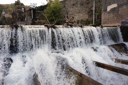 Téléchargez les photos : De puissantes chutes d'eau avec quelques branches d'arbres poussées par le fort courant sur le Tarn survolant le barrage d'Ambialet, un village pittoresque construit sur un affleurement rocheux en Occitanie, France - en image libre de droit