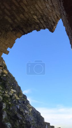 Téléchargez les photos : Ciel bleu clair vu de la voûte effondrée d'une porte fortifiée en ruines au château de Castelnau-de-Lvis, dans le sud de la France, un bastion médiéval construit en pierre brute au sommet d'une falaise rocheuse - en image libre de droit