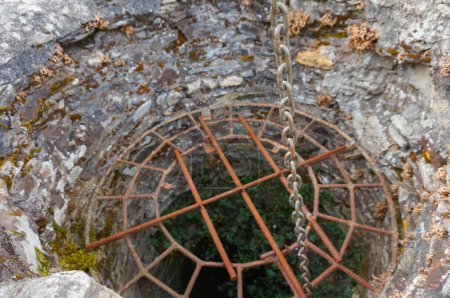 Foto de Rejilla de seguridad que cierra la boca de un antiguo pozo seco construido en piedra e invadido por plantas, en el centro de la plaza del pueblo de Villefranche d 'Albigeois, un lugar rural en el sur de Francia - Imagen libre de derechos