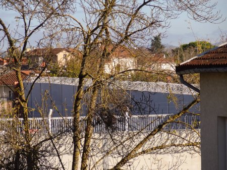 Téléchargez les photos : Albi, France - Novembre 2020 - Les murs d'enceinte en béton nouvellement construits, surmontés de fils barbelés, et la clôture métallique rigide de l'assignation à résidence locale du ministère de la Justice, cachée derrière les arbres - en image libre de droit