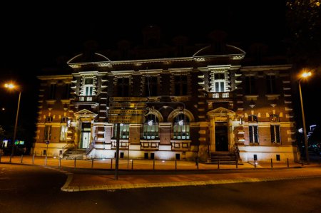 Photo for Albi, France 06, 2018 - Night shot of the illuminated Renaissance-style facade of Caisse d'Epargne agency in Jean Jaures Square, a direction sign indicating Champollion University, Cordeliers Theater - Royalty Free Image