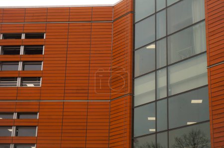 Téléchargez les photos : Détail de la façade de la Bibliothèque publique d'Albi, en France, avec un placage orange, imitation brique et de grandes baies vitrées verticales qui montrent les lumières intérieures par transparence - en image libre de droit