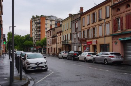 Photo for Albi, France - June 2021 - Cars parked on the curbside of Gambetta Avenue, a street bordered with typical brick, Southern townhouses and a few local businesses, near the historic city centre - Royalty Free Image