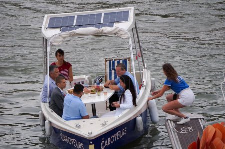 Foto de Toulouse, Francia - 30 de junio de 2023 - Una joven empleada ayuda a los clientes a atracar un barco de alquiler eléctrico, equipado con paneles fotovoltaicos, en el puerto de Viguerie en Saint-Cyprien, en el río Garona. - Imagen libre de derechos
