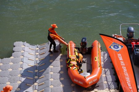 Foto de Toulouse, Francia - 2 de julio de 2023 - Un salvavidas del SNSM carga el equipo en un bote naranja e inaplanable; hay otro bote salvavidas en el muelle, que flota en el río Garona, junto al puerto de Daurade - Imagen libre de derechos