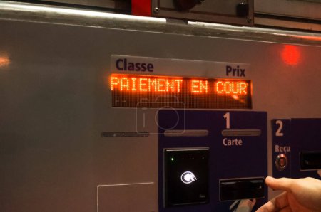 The screen of a payment terminal in a tollgate in France displaying "ongoing payment", indicating that the transaction is being processed, with the stretched hand of a man waiting for his credit card