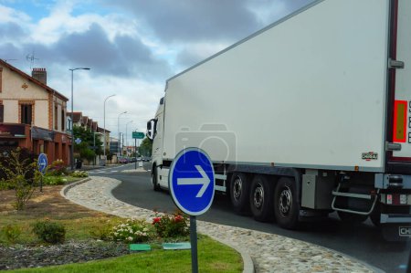 Téléchargez les photos : Albi, France - Sept. 2020 - Un camion de livraison blanc (une semi-remorque du constructeur suédois Volvo Trucks), manœuvrant dans le passage étroit d'un rond-point paysager, tout en traversant la ville - en image libre de droit