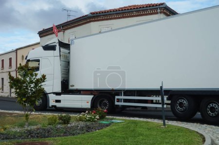 Foto de Albi, Francia - Sept. 2020 - Un camión de reparto blanco (un semirremolque del fabricante sueco Volvo Trucks), operado por un transportista de motor, maniobra en un paso estrecho de una rotonda ajardinada - Imagen libre de derechos
