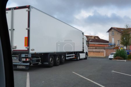 Photo for Albi, France - Sept. 2020 - A white, long truck in motion, towing a refrigerated trailer made by the French manufacturer Chereau, maneuvers in a retail store parking lot after the morning delivery - Royalty Free Image