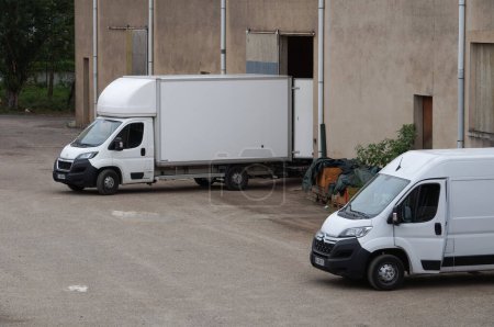 Téléchargez les photos : Albi, France - Juillet 2022 - Camionnettes mobiles Citroën et Peugeot blanches en position renversée, déchargeables, les portes ouvertes, devant les portes coulissantes d'une unité de stockage servant de dépôt de meubles - en image libre de droit