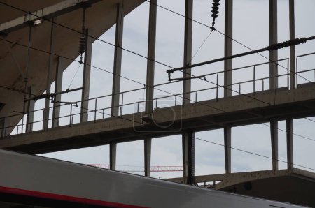 Foto de Reims, Francia - abril de 2021 - Catenaria de trenes eléctricos en primera línea, y estructura de hormigón que sostiene el techo arqueado de la estación ferroviaria Gare de Reims Centre, en el fondo - Imagen libre de derechos